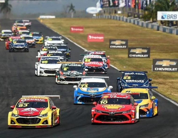 Corrida da Stock Car em pista de autódromo com vários carros competindo em alta velocidade, representando etapa da Stock Car em Cuiabá.